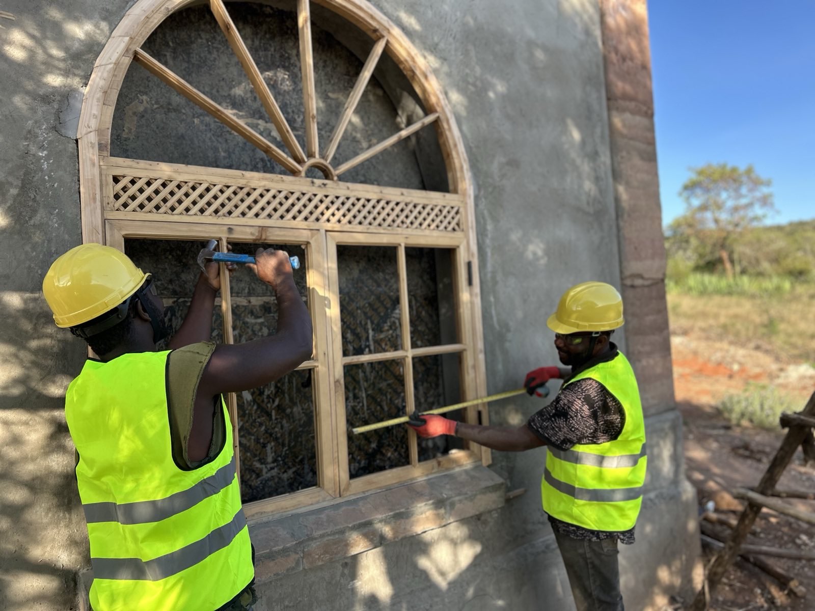 Savanna Builders craftsmen installing custom wooden door frame with decorative lattice work